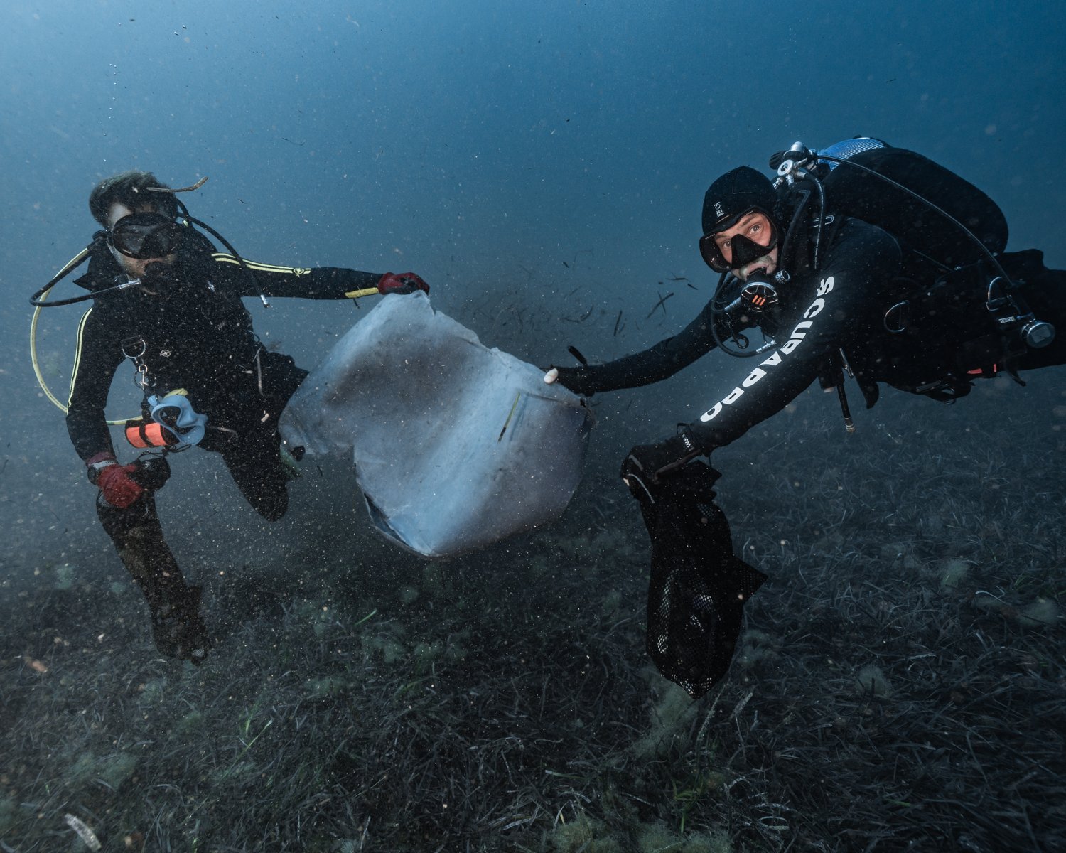 Two divers carrying a torn-up oil tank off the seabed during the Exiles reef clean-up dive in Sliema, Malta