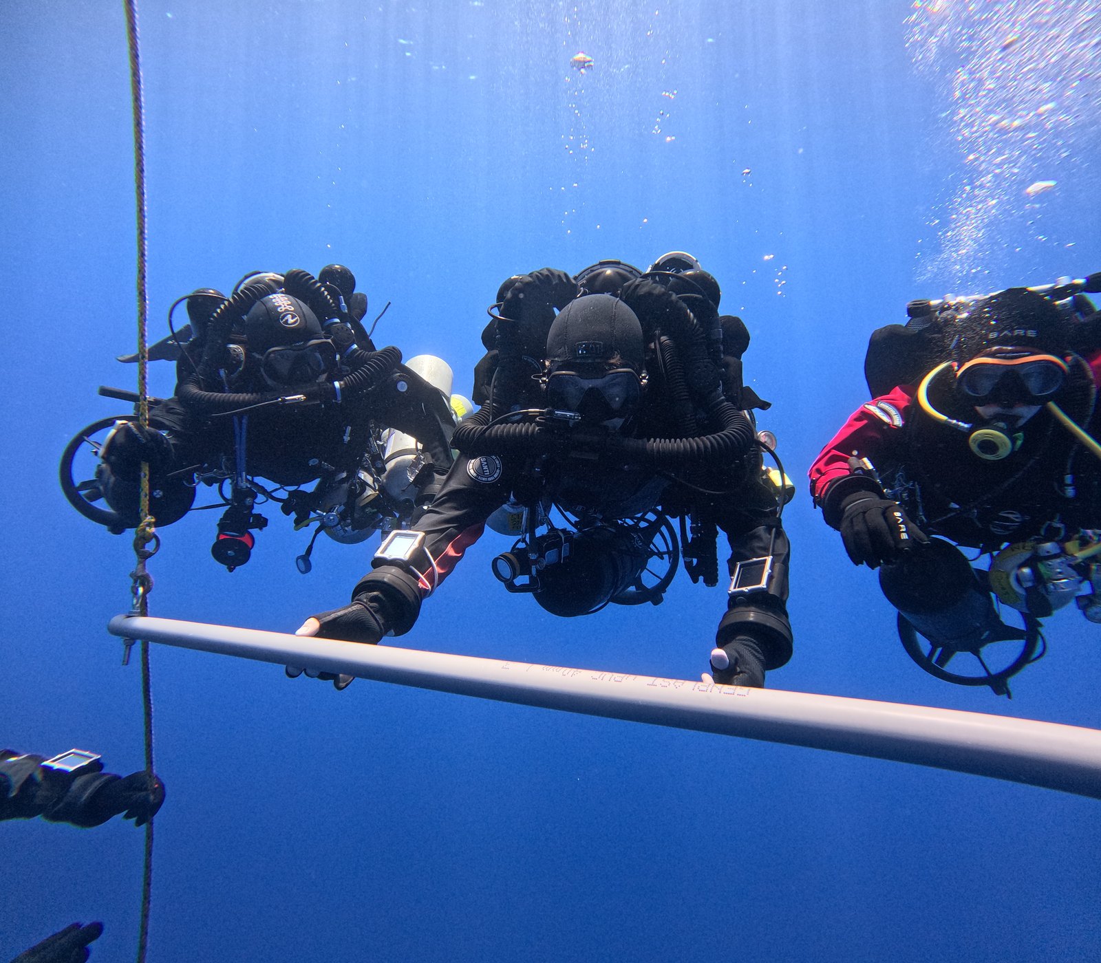 A team of technical divers on a deco bar in clear blue water in Malta
