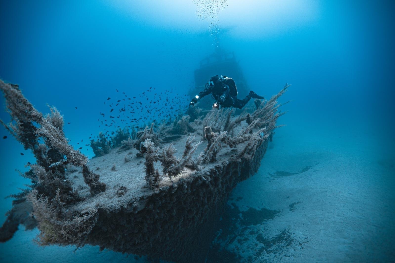 A diver over the bow of the P29 patrol boat wreck at Cirkewwa, Malta, superstructure behind