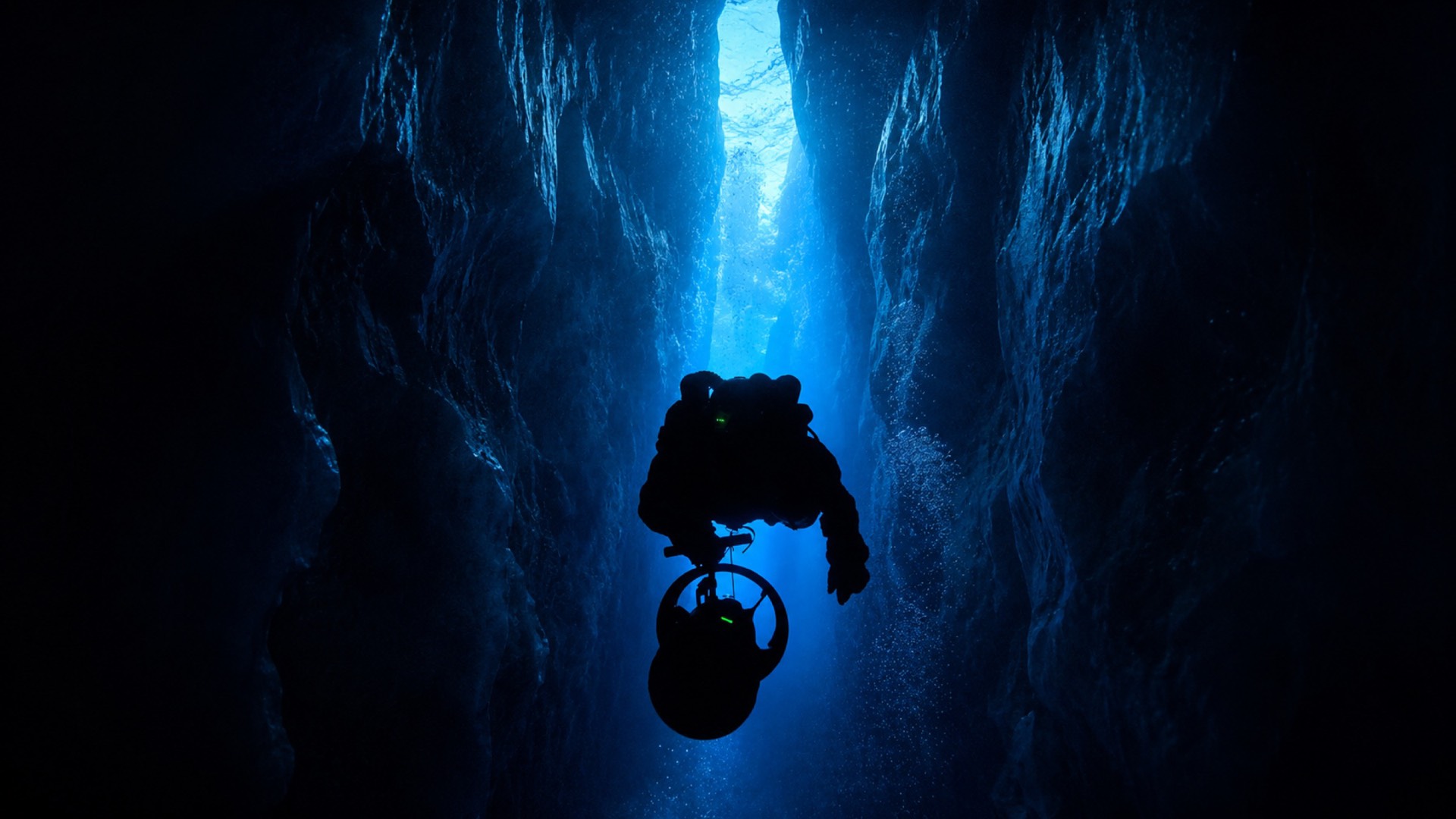 A technical diver descending through a narrow cavern towards the light
